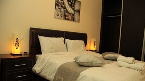 Ein ordentlich bezogenes Bett mit weißer und grauer Bettwäsche, zwei Nachttischlampen und ein Wandbild darüber.