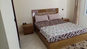 Une chambre à coucher avec un cadre de lit en bois, une couvre-lit à motifs, deux oreillers, une table de chevet et une commode.