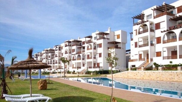 Ein Resort mit mehreren weißen Gebäuden, einem Swimmingpool und Liegestühlen auf einer Rasenfläche.