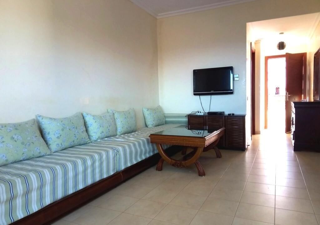 A living room with a sofa, a coffee table, and a flat-screen TV mounted on the wall.