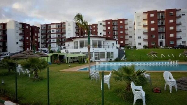 Ein Mehrfamilienhaus mit mehreren Stockwerken, einem Swimmingpool und Außenmöbeln.