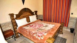 Un dormitorio con cama de madera, pared de ladrillo, cortina a rayas y una mesita de noche de madera.