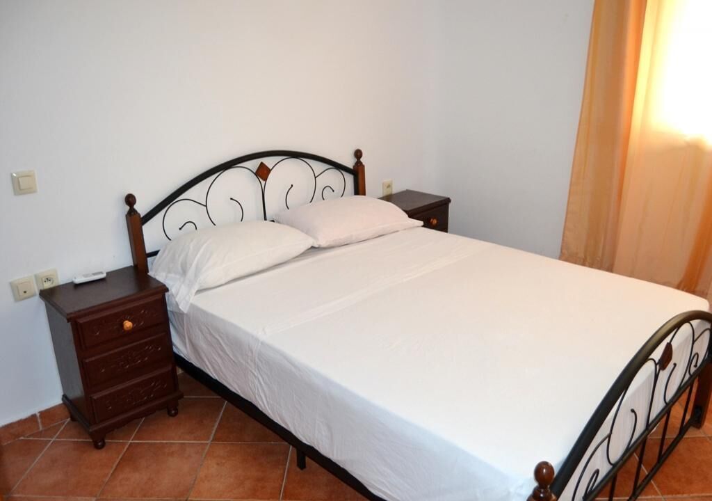 A single bed with a metal frame and wooden headboard, accompanied by a nightstand with drawers and a small table.