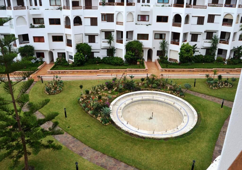 Ein mehrstöckiges Hotel mit Innenhof, der einen kreisförmigen Brunnen, gepflegte Rasenflächen und verschiedene Pflanzen umfasst.