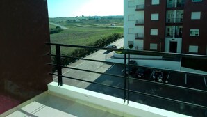 Une vue depuis un balcon donnant sur un parking et un immeuble à plusieurs étages, lui aussi doté de balcons.