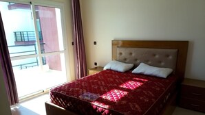 Une chambre dotée d’un grand lit, d’une table de chevet, d’une commode et d’une porte-fenêtre coulissante donnant sur un balcon extérieur.