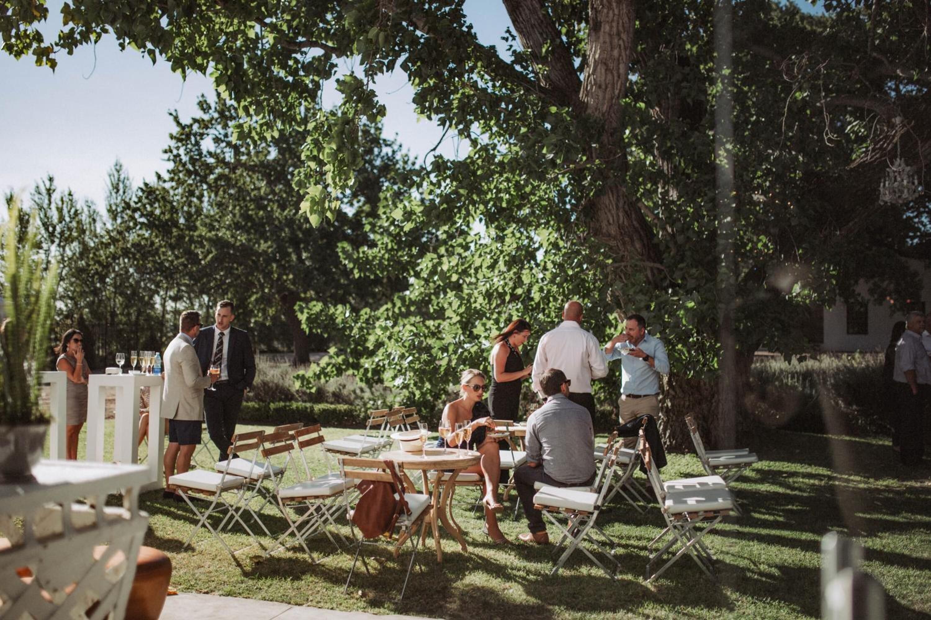An outdoor gathering with people seated at tables under trees.