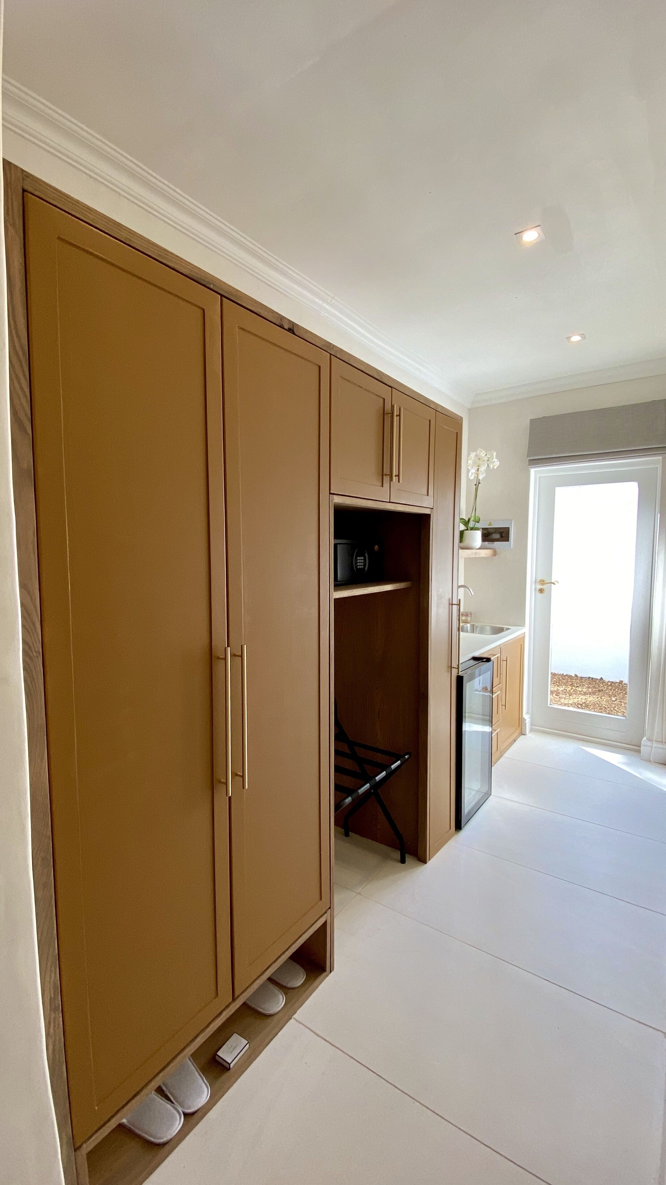 A spacious room with a large wardrobe, a small kitchen area, and a door leading to a balcony.