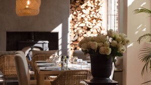 A dining area with wicker furniture, a table set for two, and a vase of white flowers. - La Paris Estate (Franschhoek)