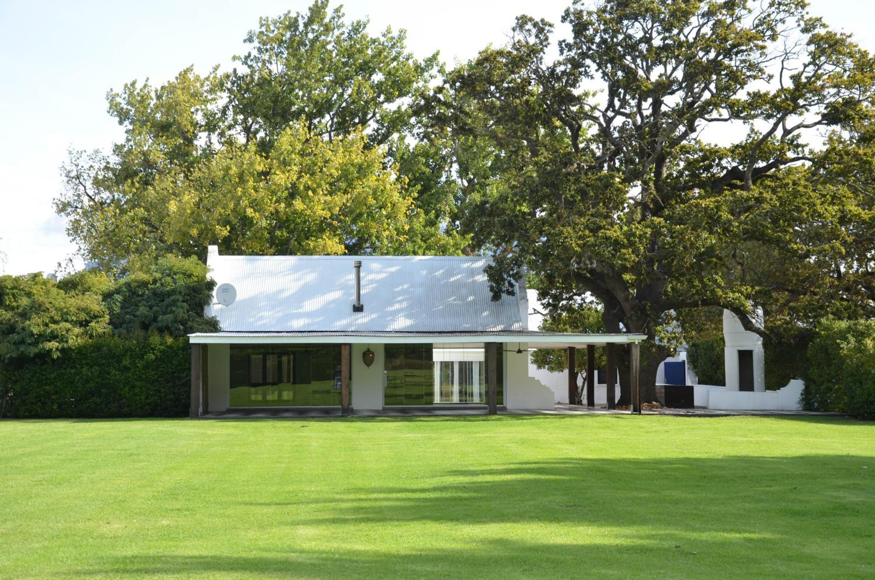 A modern house with a large lawn in front, surrounded by trees.