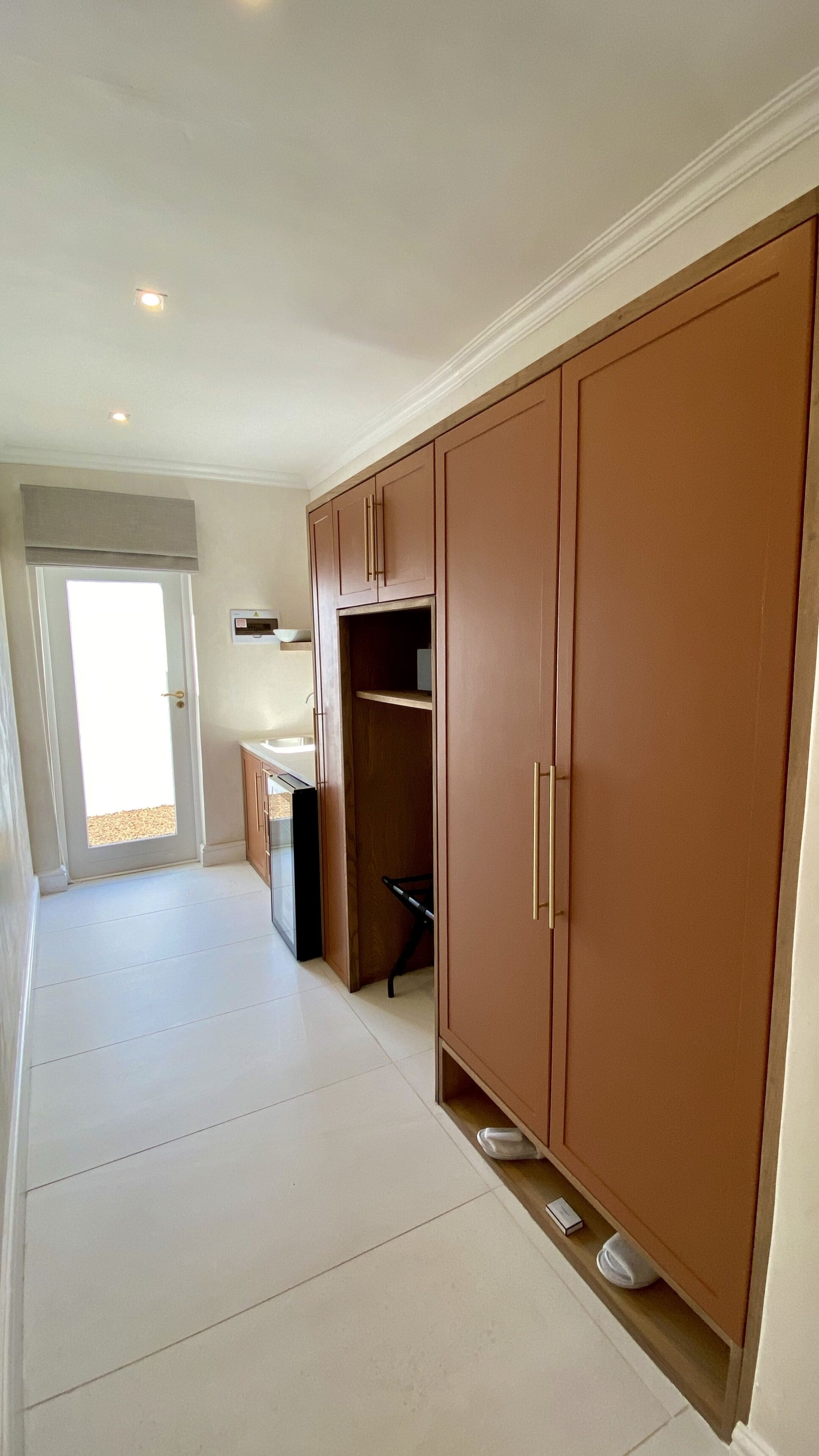 A hallway with a kitchen area, wooden cabinets, and a door leading outside.