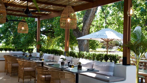 An outdoor dining area with wicker furniture, a long table, and hanging lights. - La Paris Estate (Franschhoek)