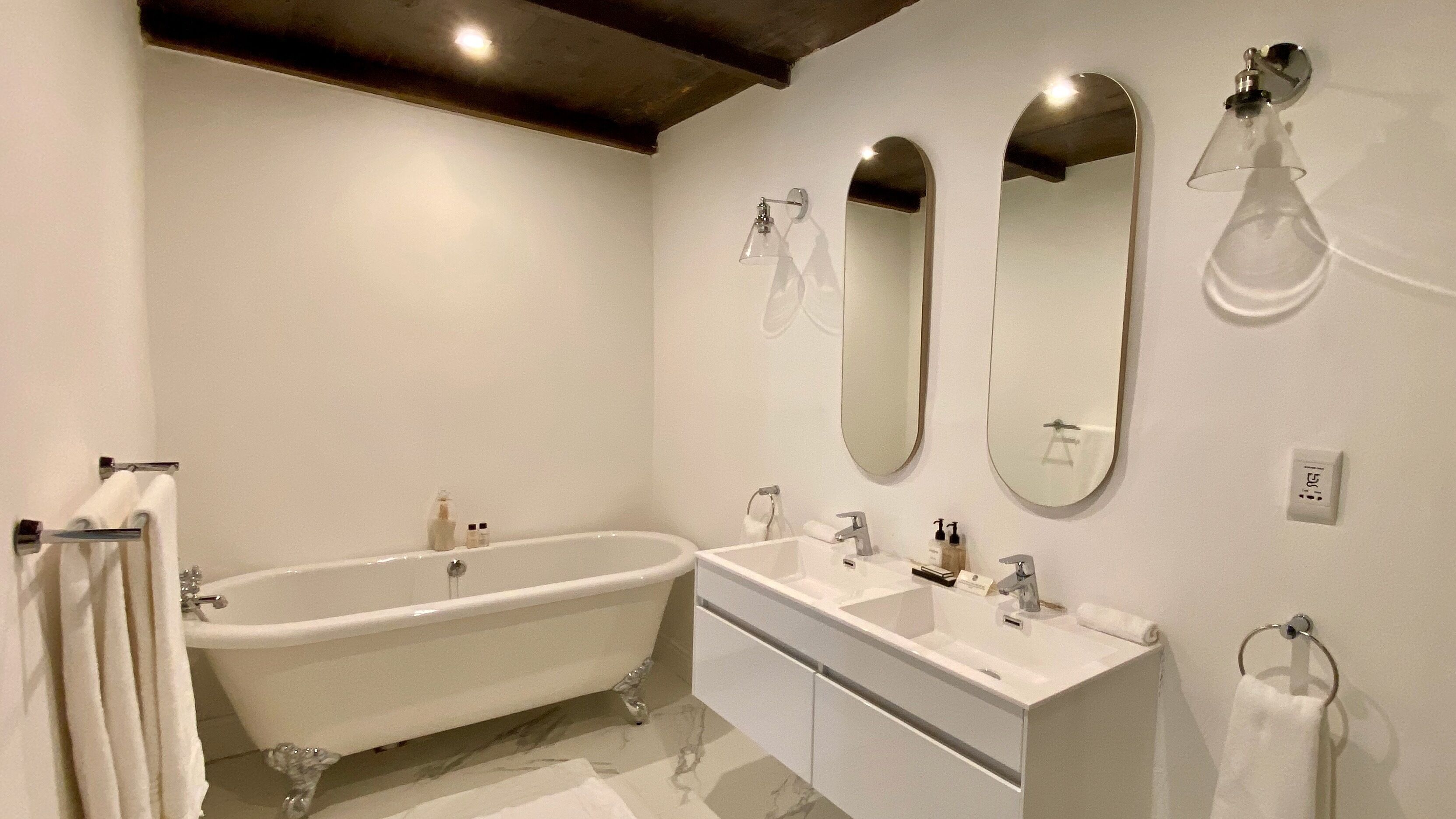 A bathroom with a freestanding bathtub, two sinks, and three mirrors.