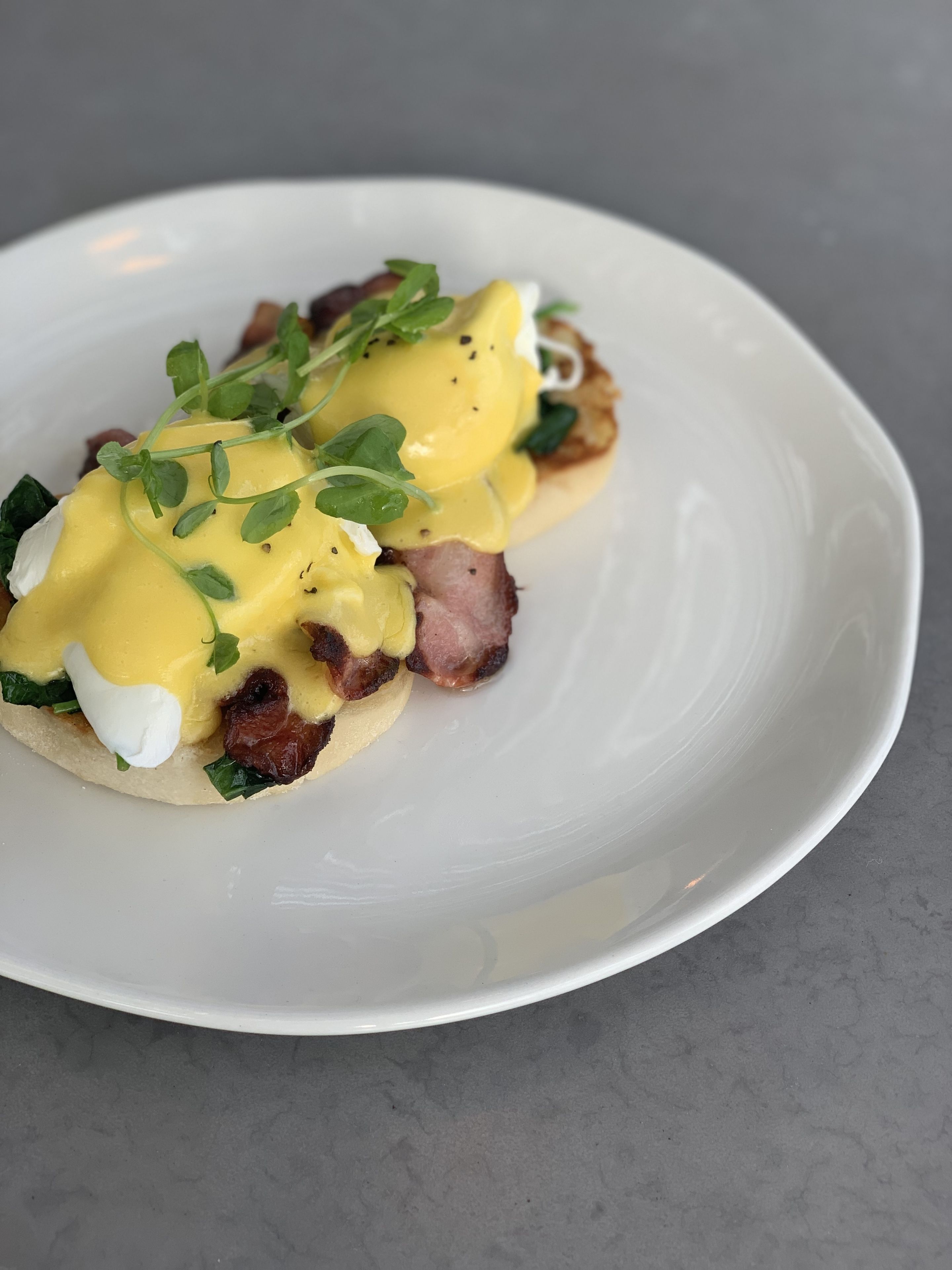 A plate with a breakfast dish consisting of eggs, bacon, and greens.