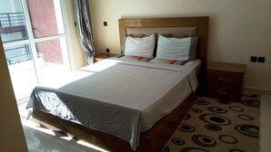 A neatly made bed with a wooden headboard, a bedside table with a lamp, and a patterned rug on the floor. - Ocean Atlantic Residence 3050 (Asilah)