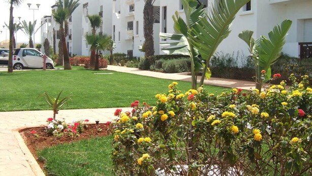 Edifício residencial com várias varandas, gramado bem cuidado e diversos vasos de flores.