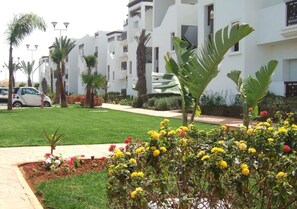 A residential building with multiple balconies, a well-maintained lawn, and a variety of flowering plants. - The Greens Residence 3615 (SAIDIA)