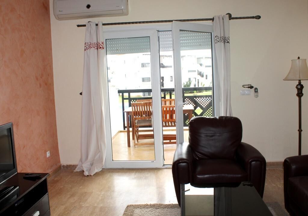 Une pièce dotée d’une porte-fenêtre coulissante donnant sur un patio extérieur, d’un fauteuil en cuir, d’un téléviseur et d’une lampe.