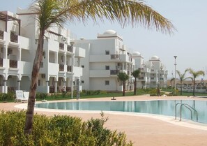 Un resort con varias edificaciones blancas, una piscina y palmeras.
