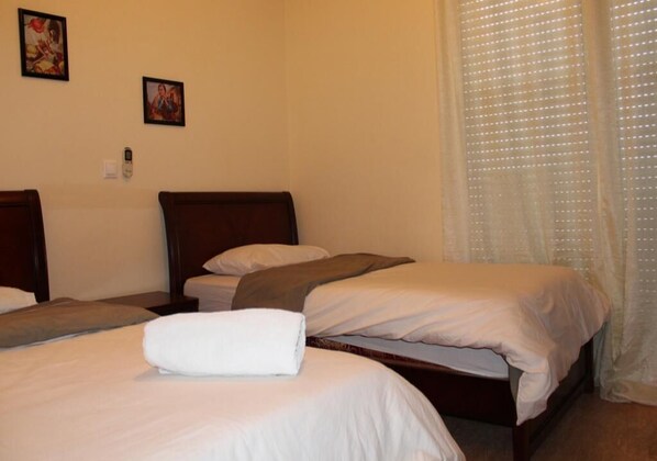 Habitación de hotel con tres camas individuales, cabecera de madera y cortina estampada de lunares.