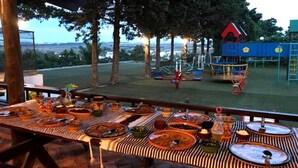 Un espace de restauration en plein air, avec une table dressée pour un repas, donnant sur une aire de jeux dotée de différents équipements.
