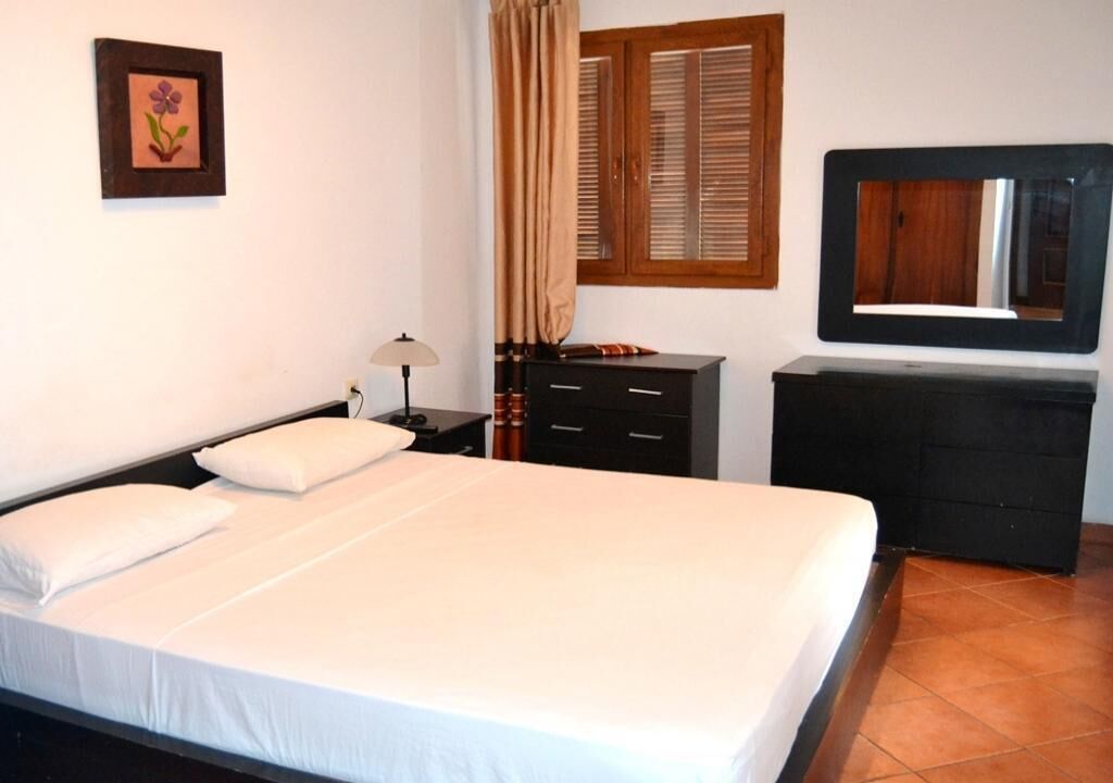 A neatly arranged bedroom with a bed, a dresser, a mirror, and a window with curtains.