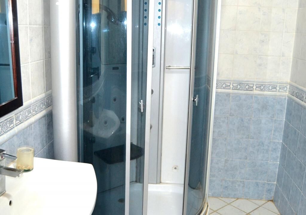 Een badkamer met een douchecabine, een wit wastafel en een spiegel.
