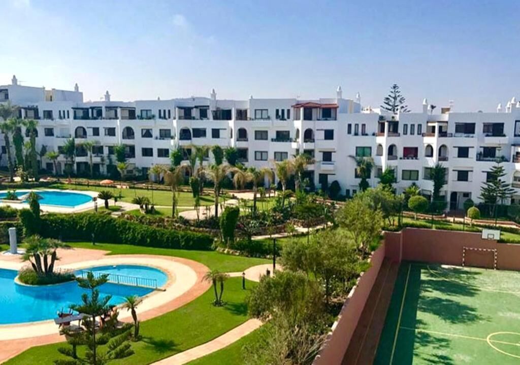 Un hôtel composé de plusieurs bâtiments blancs, doté d’une piscine et d’un court de tennis.