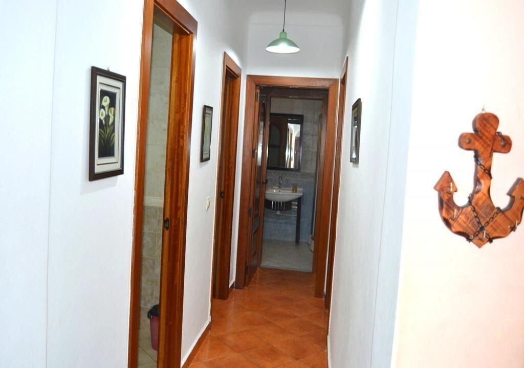 A narrow hallway with wooden doors, a tiled floor, and a hanging pendant light.