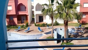 Vue d’une cour d’hôtel avec des palmiers, des chaises longues et une piscine.