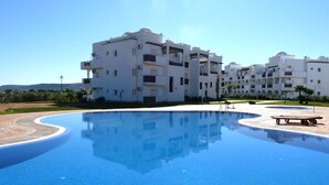 A modern hotel with a large swimming pool, white buildings, and a clear blue sky. - The Greens Residence 3623 (Saidia)