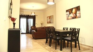 A dining area with a table and chairs, a sofa, and a painting on the wall. - The Greens Residence 3623 (Saidia)