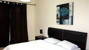 A neatly made bed with white linens, a dark headboard, and a small bedside table with a lamp. - The Greens Residence 3623 (Saidia)