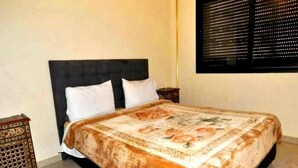 A neatly made bed with a floral bedspread, a small wooden side table, and a patterned rug on the floor. - Residence Babylon Marrakech 3418 (Marrakech)