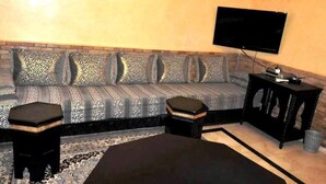Una sala de estar con un sofá, dos otomanas, una mesa de centro, un televisor y una mesita auxiliar.