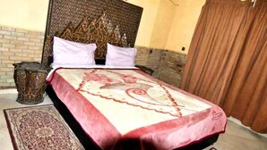 Una cama con cabecera estampada, una colcha beige y roja, y almohada a juego.