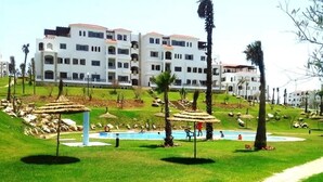 A hotel with multiple white buildings, a swimming pool, and a grassy area with palm trees. - Lilac's Garden Residence 2947 (Cabo Negro)