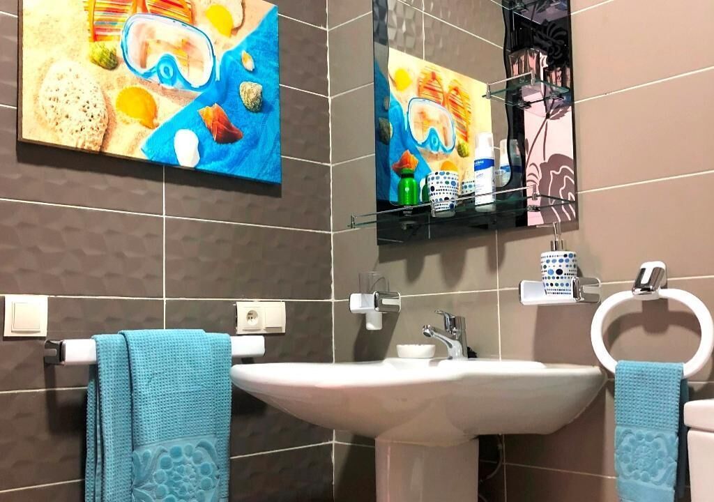 A bathroom with a large sink, two towels, a mirror, and a shelf with toiletries.