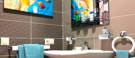 A bathroom with a large sink, two towels, a mirror, and a shelf with toiletries.