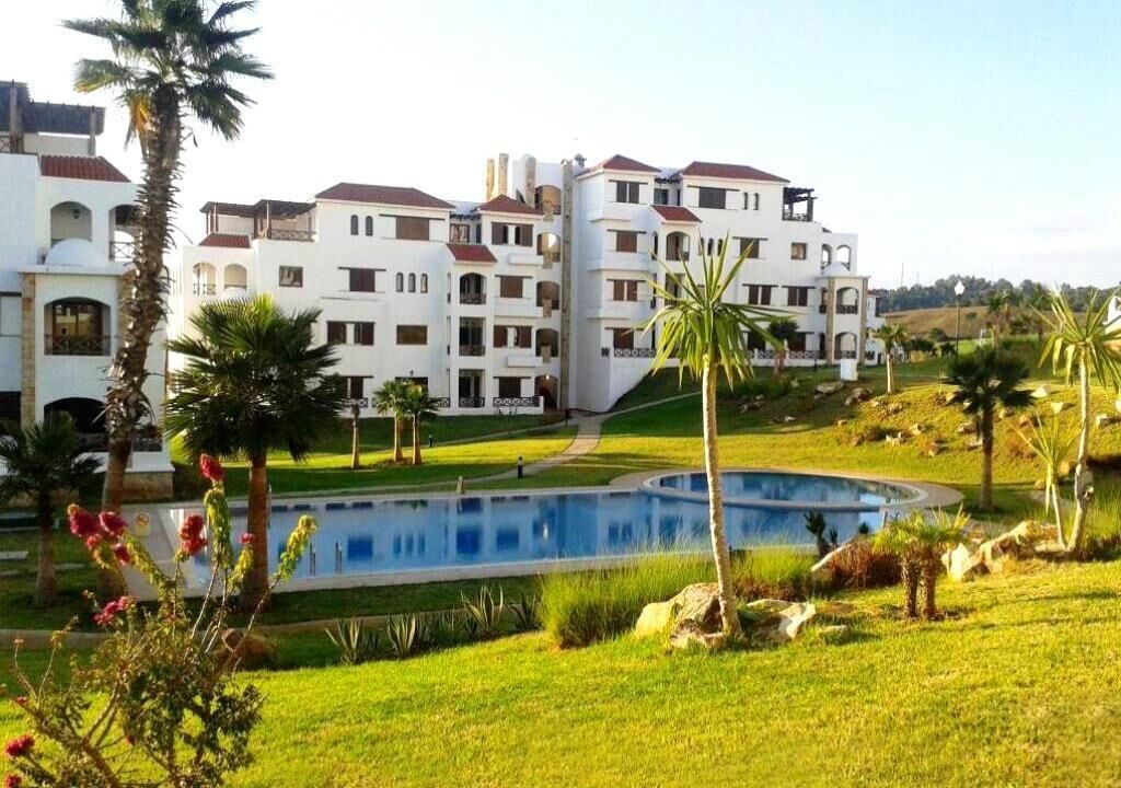 A multi-story hotel with a swimming pool, surrounded by palm trees and greenery.