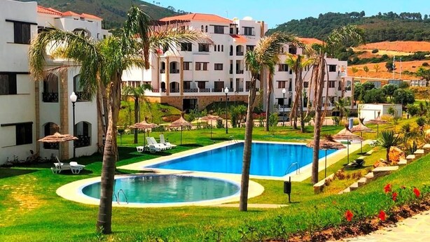 A hotel with a swimming pool, palm trees, and a hilly backdrop. - Lilac's Garden Residence 2947 (Cabo Negro)