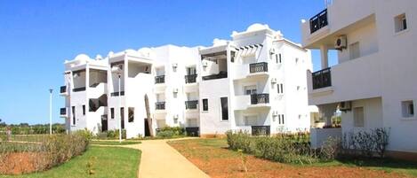 A modern apartment complex with multiple balconies, a central pathway, and a well-maintained lawn.