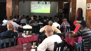 Ein Restaurant mit Gästen an Tischen, einem großen Bildschirm, der ein Sportereignis zeigt, und einer Kandelaber-Leuchte an der Decke.