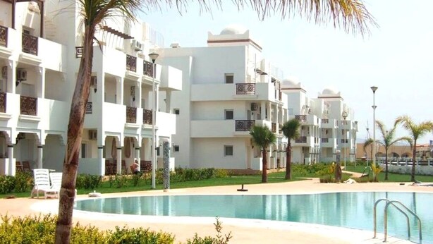 Een resort met een zwembad, palmbomen en witte gebouwen met balkons.