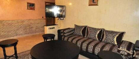 A living room with a sofa, two round tables, a flat-screen TV, and a fireplace.