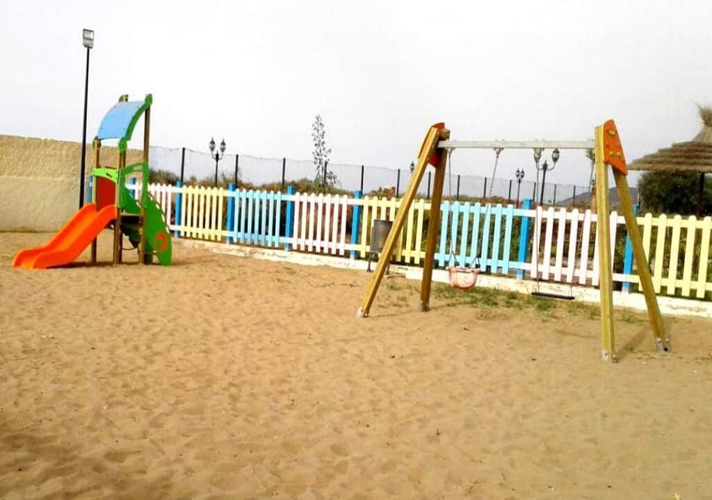A playground with a slide and swings, surrounded by a white picket fence.
