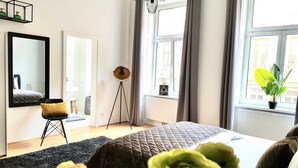 Ett sovrum med en stor säng, en golvlampa, en krukväxt och utsikt över staden genom fönstret.