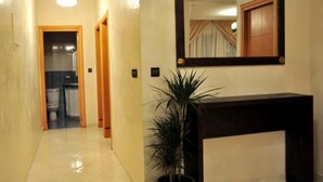 A hallway with a potted plant, a mirror, and a wooden door leading to a bathroom. - Residence Amwajiagadir 1932 (Agadir)