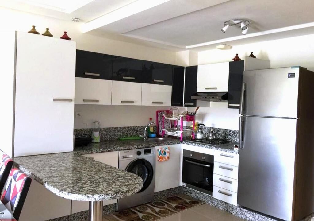 Uma cozinha compacta com máquina de lavar, geladeira e micro-ondas.