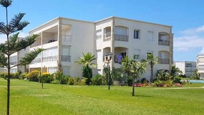 A multi-story building with balconies, surrounded by a well-maintained lawn and palm trees. - Residence Olavonka 3364 (CASABLANCA)